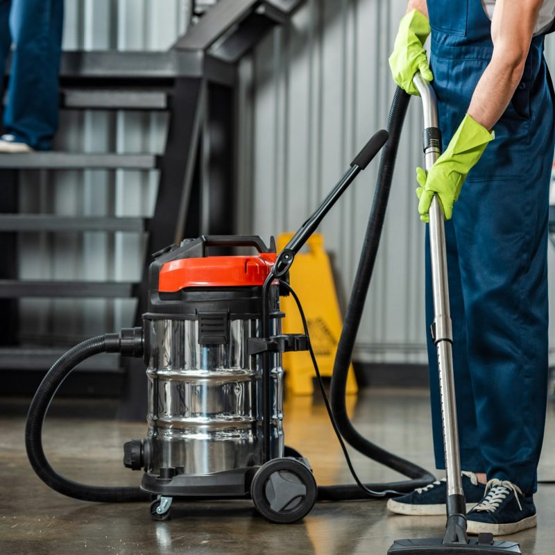 cropped view of cleaner in uniform cleaning floor with vacuum cleaner